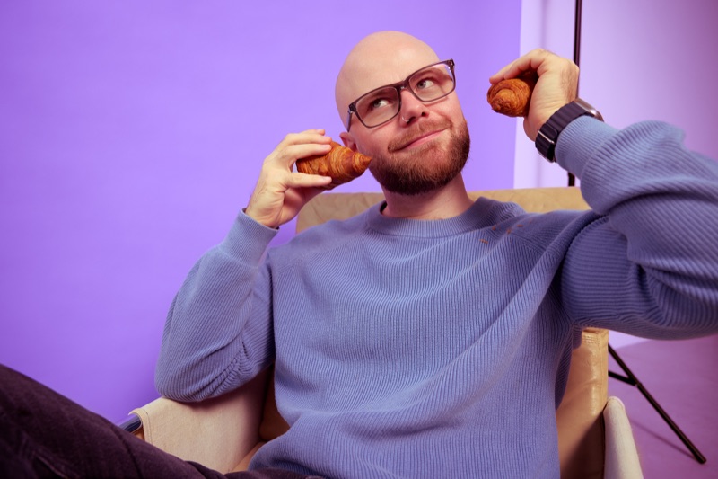 Rubin Koot sits in a chair with a croissant at each ear, looking up as if listening