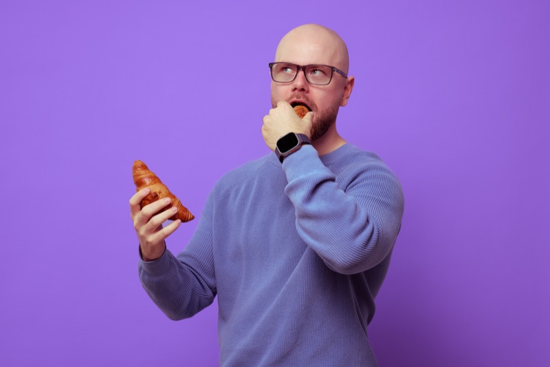 Rubin Koot neemt een hap en kijkt peinzend omhoog, met een croissant in zijn andere hand