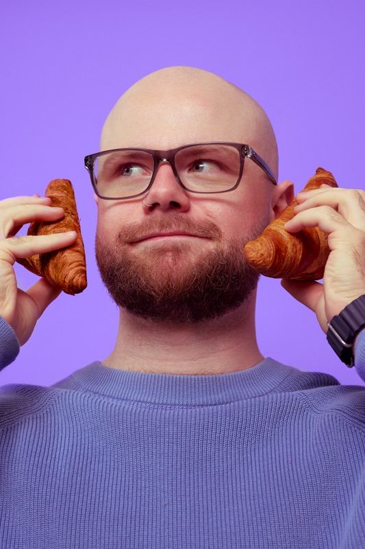 Rubin Koot houdt twee croissants tegen zijn oren en kijkt luisterend omhoog