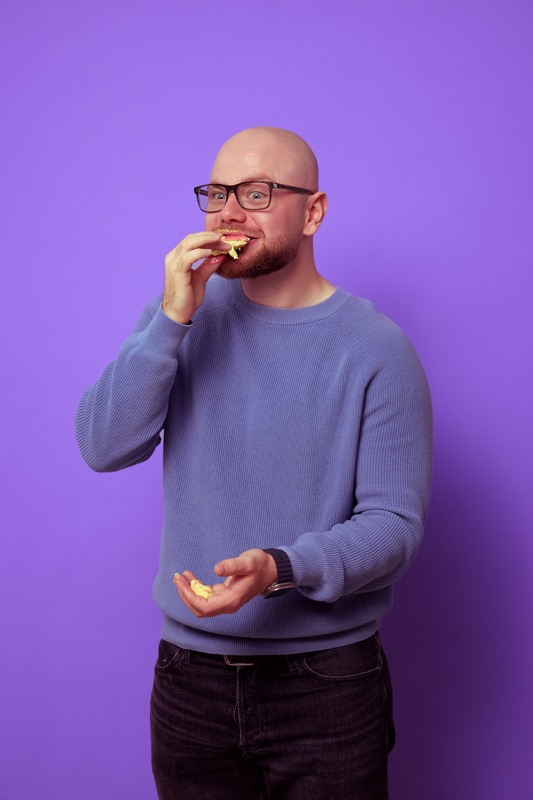 Rubin Koot staat lachend met een gebakje in zijn hand en neemt een hap