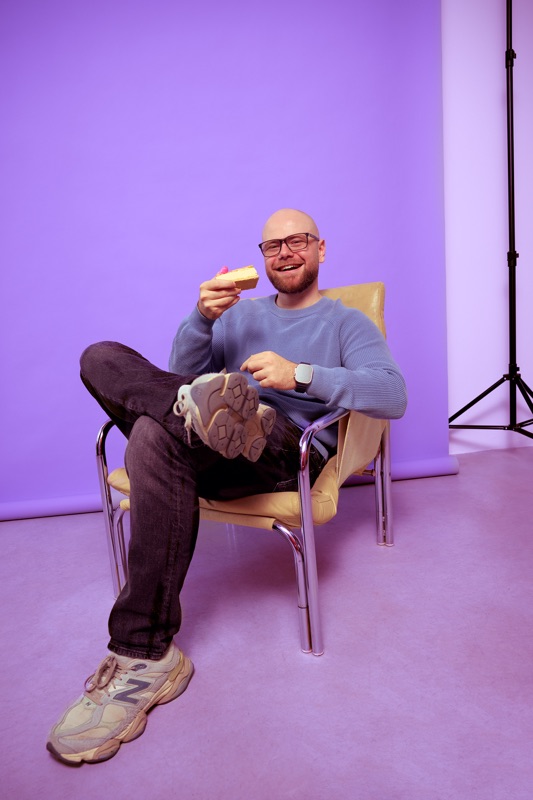 Rubin Koot zit ontspannen op een stoel met een gebakje in zijn hand